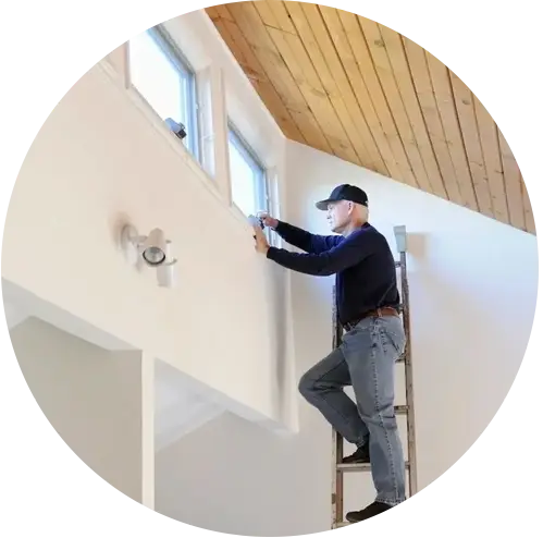 A man on a ladder painting the ceiling of a room.